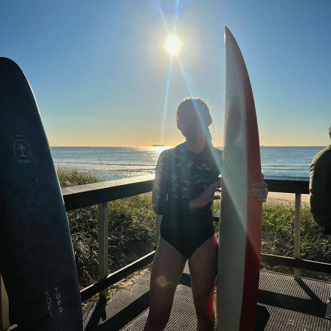Jente poserer med surfebrett i solnedgang
