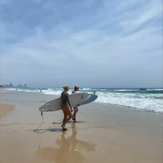to personer står med surfebrett under armen og ser utover havet