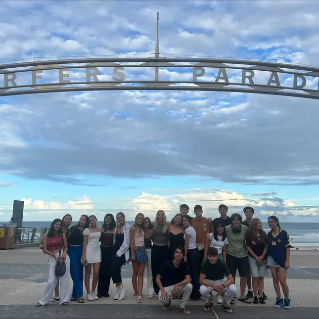 En gjeng utvekslingselever står i en klynge ved stranda under et skilt med ordene "surfernes paradis".