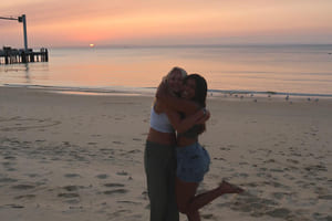 To venninner klemmer på stranda med en solnedgang i bakgrunnen