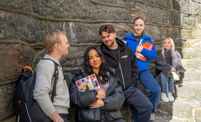 Fem elever henger i gruppe med en steinmur bak seg.