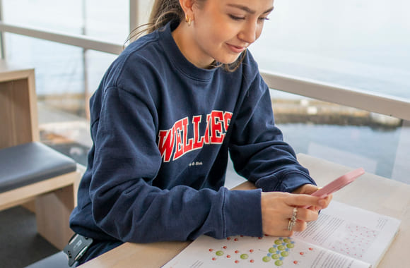 En privatist leser i en pensumbok mens hun kikker på telefonen