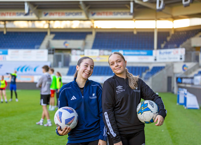 To elever på fotballbanen med hver sin fotball under armen.