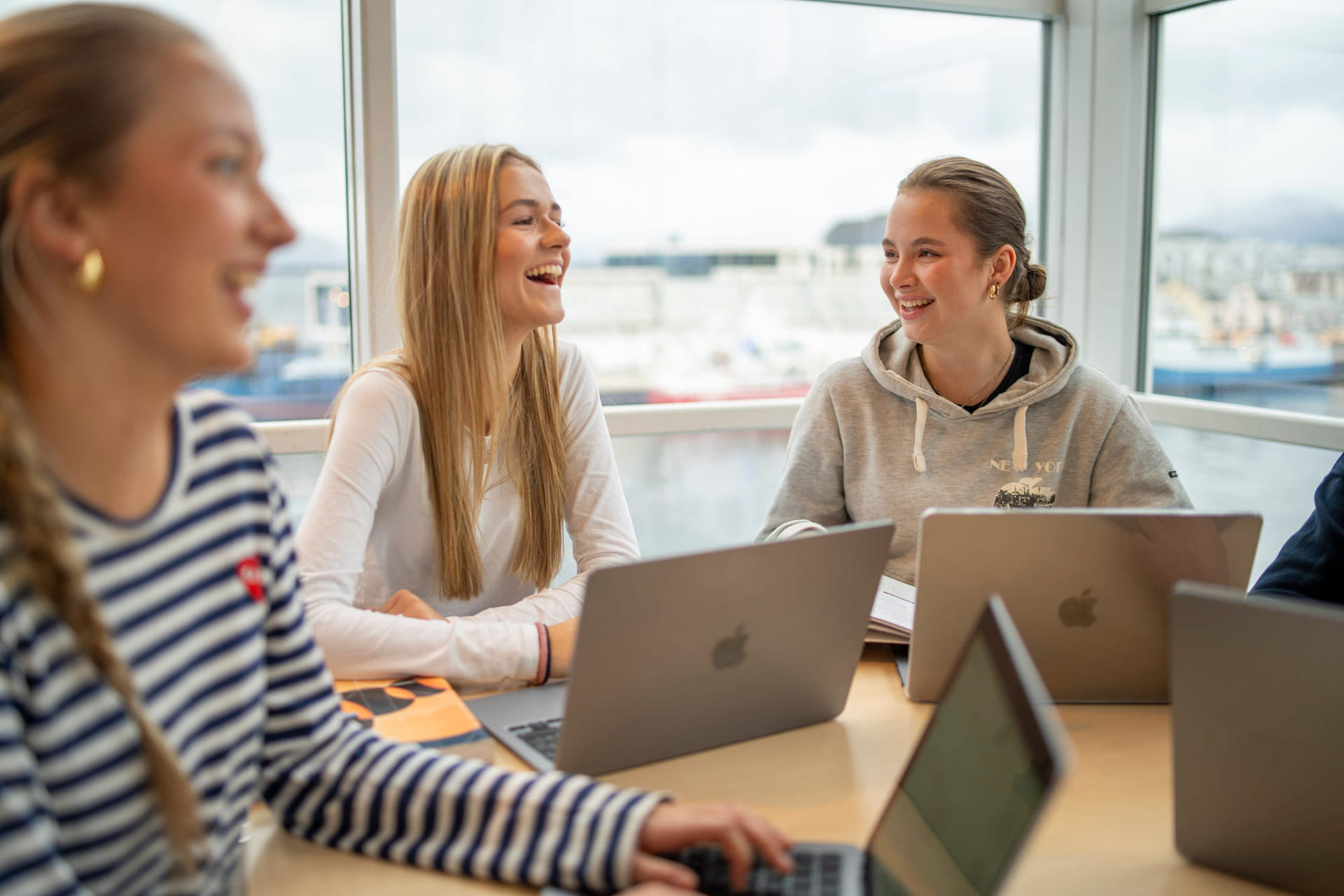 Tre elever snakker sammen med macbook på akademiet