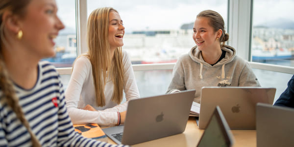 Tre elever snakker sammen med macbook på akademiet