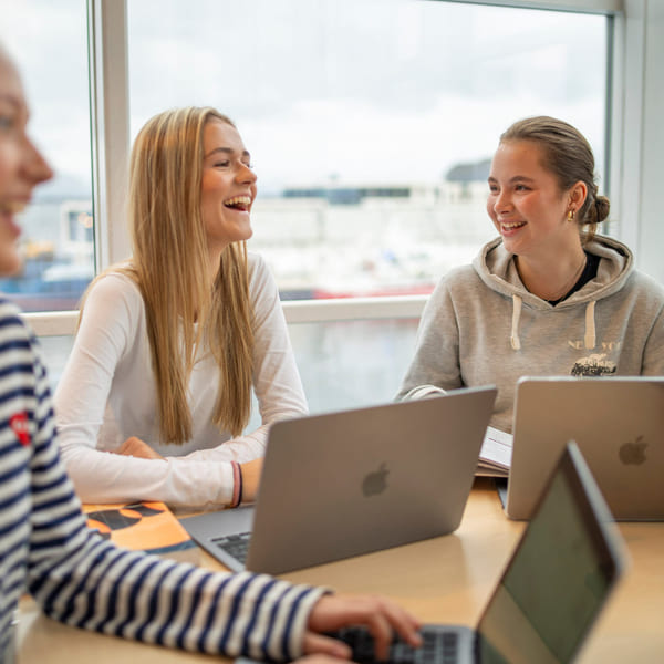 Tre elever snakker sammen med macbook på akademiet