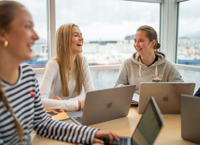 Tre elever snakker sammen med macbook på akademiet
