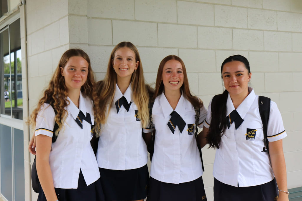 Fire elever på Coolum SHS holder rundt hverandre og smiler til kamera utenfor skolen.