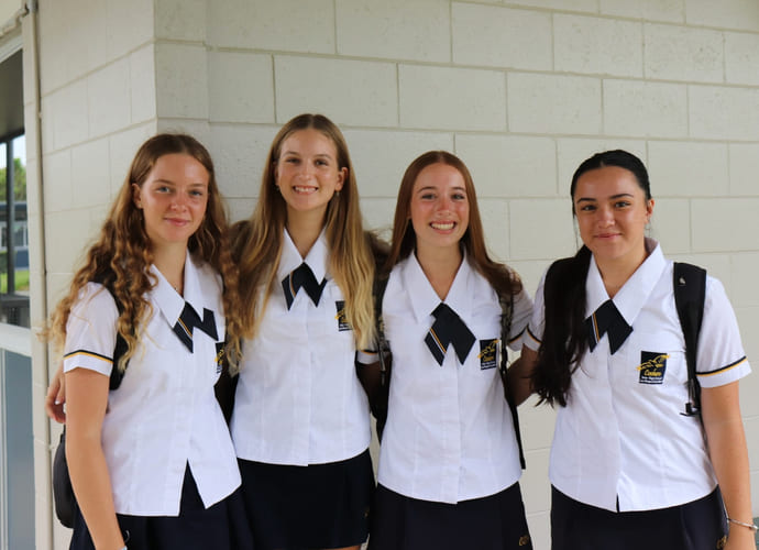 Fire elever på Coolum SHS holder rundt hverandre og smiler til kamera utenfor skolen.