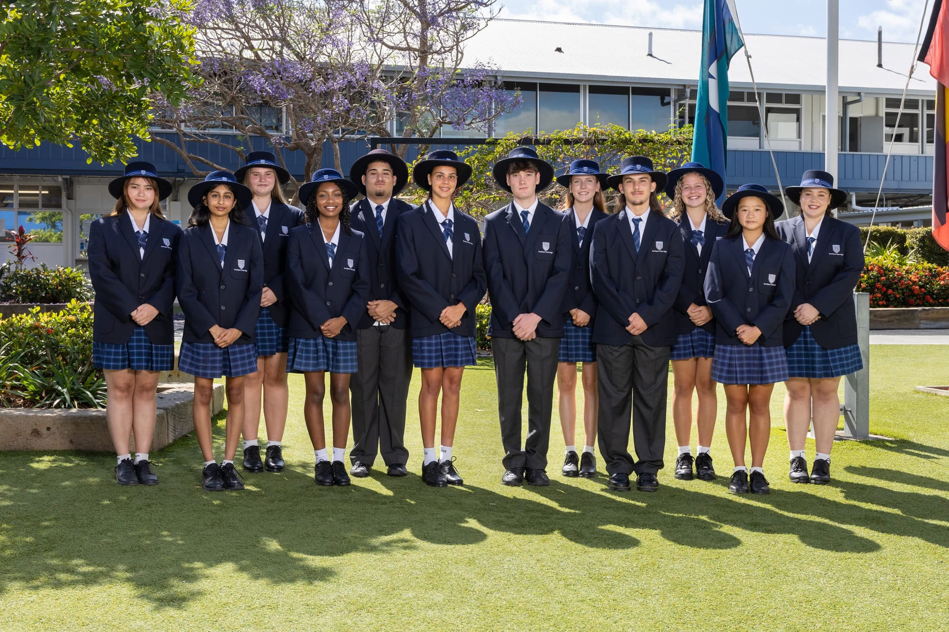 En stor gjeng med elever på Southport State High School står i skoleuniform utenfor skolen og smiler.