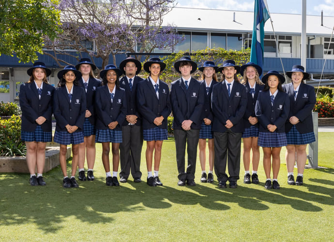 En stor gjeng med elever på Southport State High School står i skoleuniform utenfor skolen og smiler.