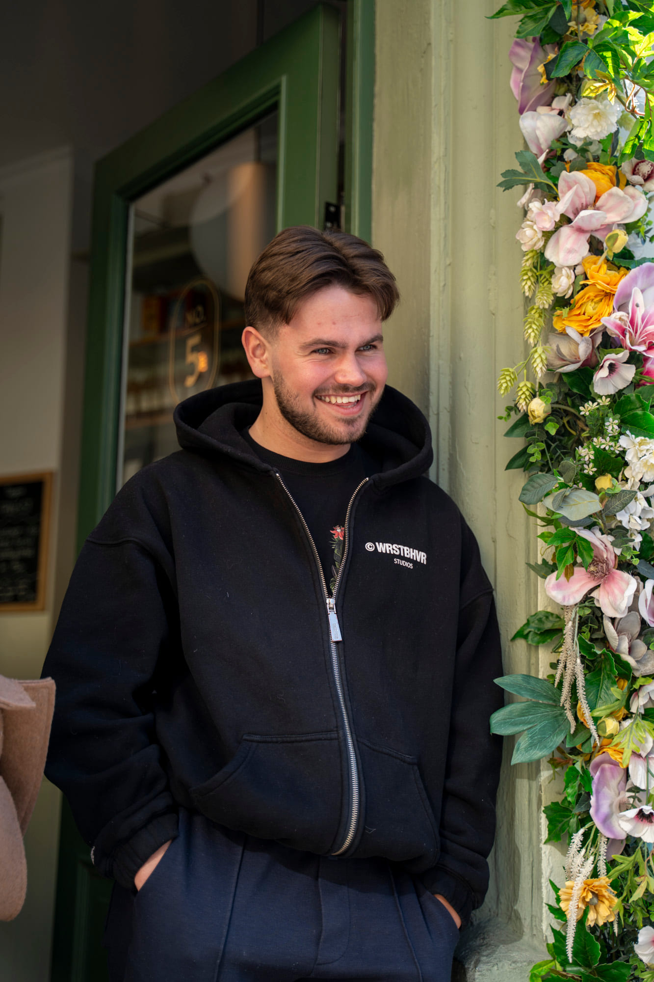 Gutt står i døra på en kafe med blomster i bakgrunn
